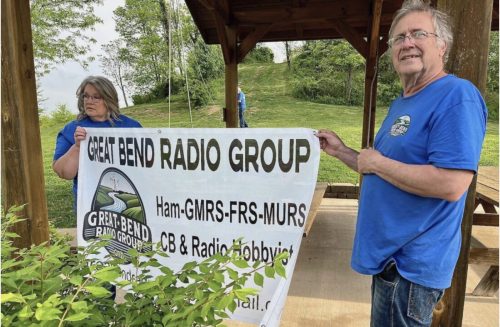 Man and woman hanging banner at park gazebo.